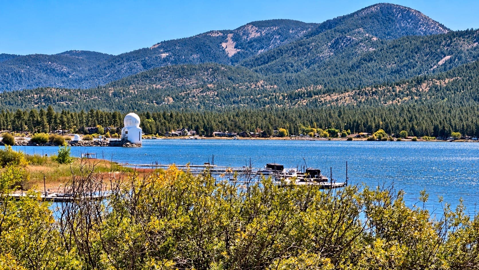 Big Bear Lake shoreline with boat docks and forested mountains under a blue sky