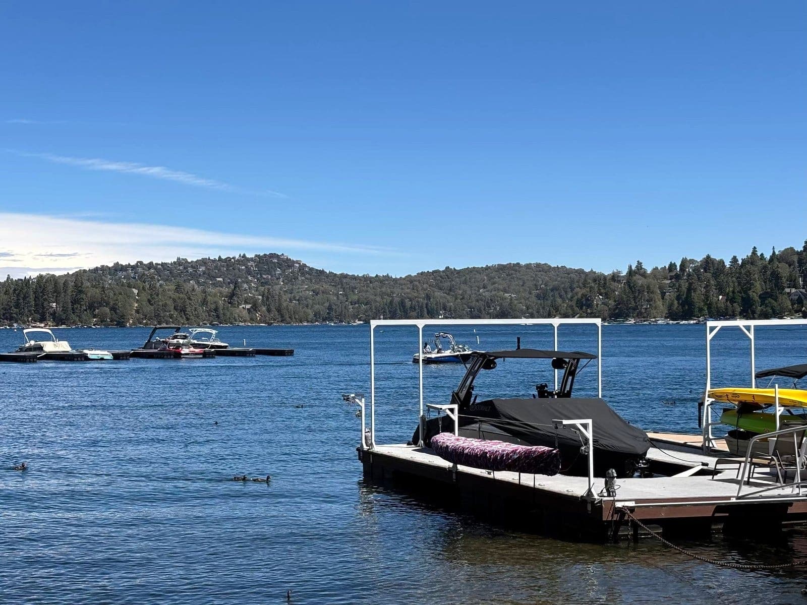 A covered motorboat and kayaks tied at a dock on Lake Arrowhead.