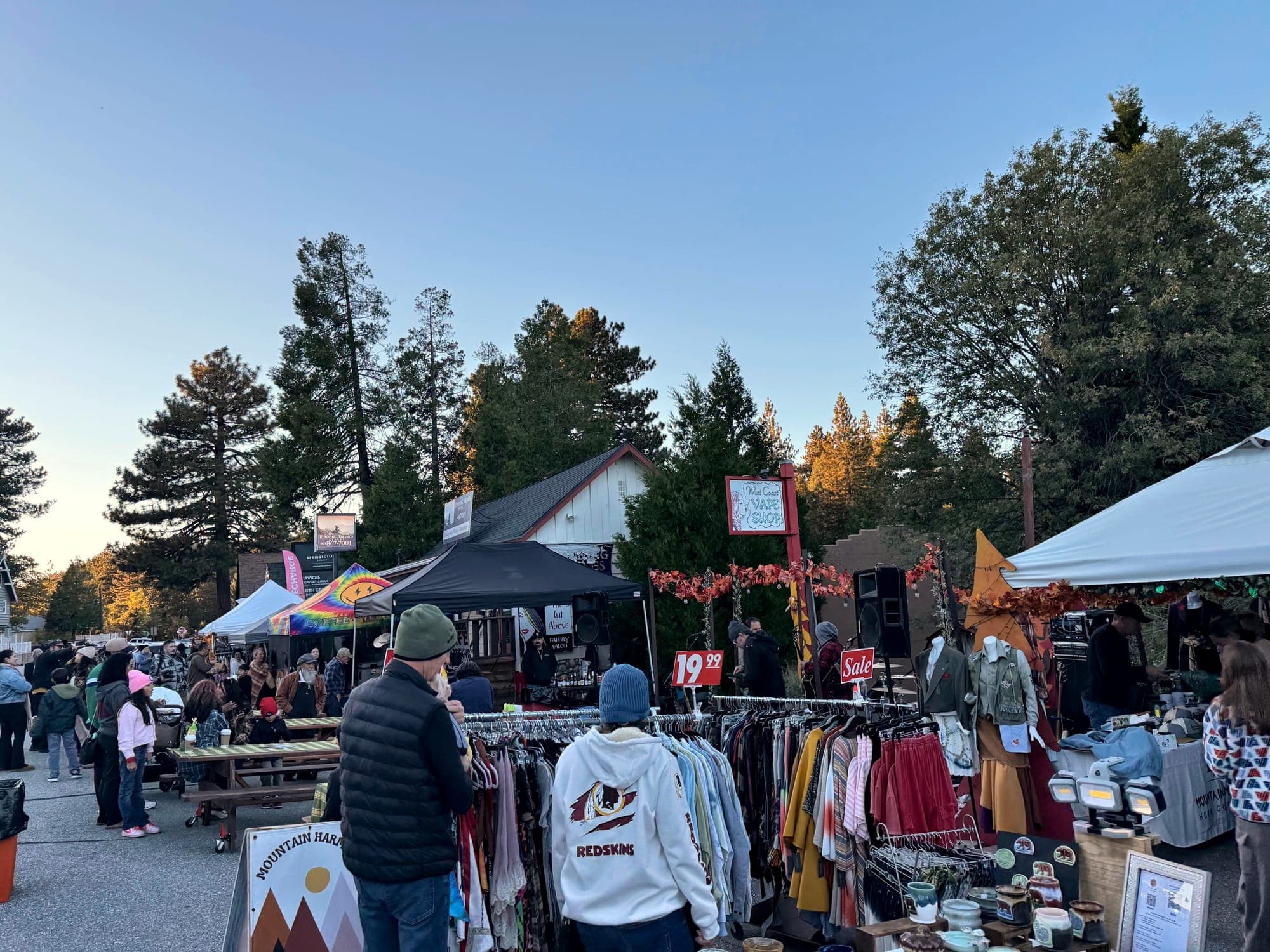 Row of vendor tents and shoppers under pines at a Running Springs community event