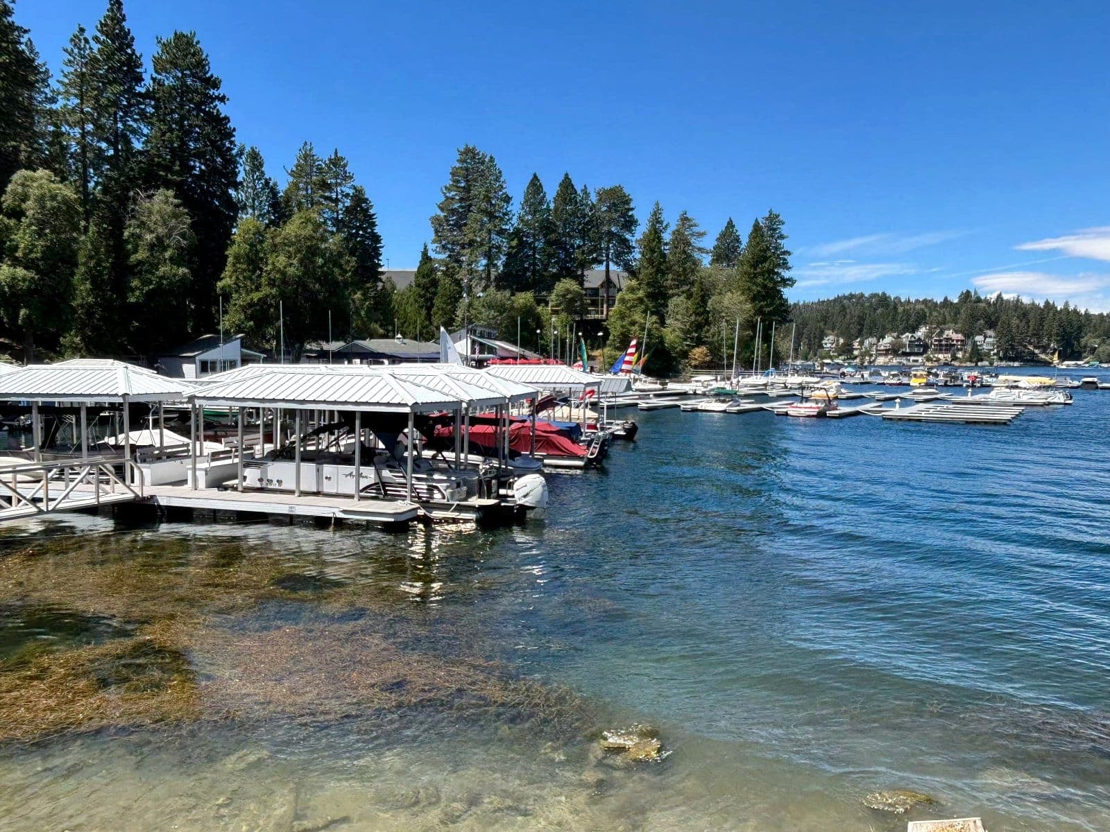 Covered wooden boat slips on Lake Arrowhead with pine forest behind them.